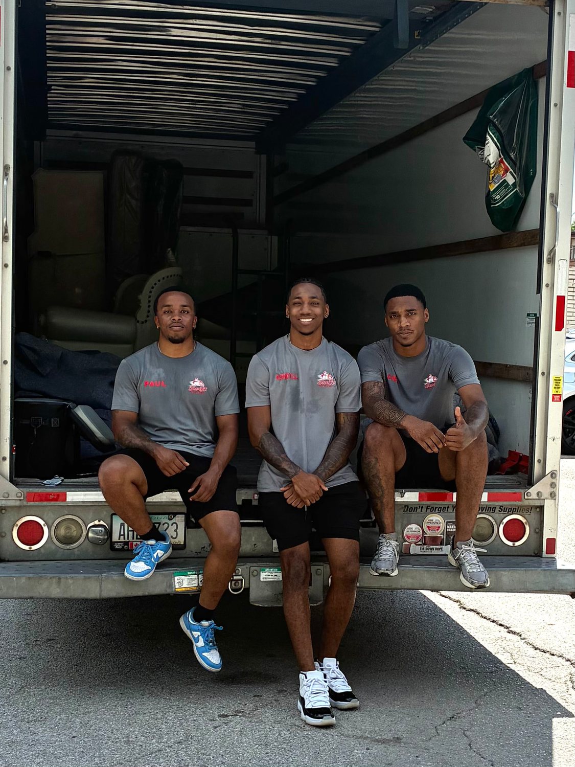 Swift Movers crew resting on the tail of a truck packed with wrapped furniture